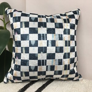 Puede incluir: Una almohada de tiro de cuadros negros y blancos con un sutil brillo iridiscente. La almohada tiene un patr&oacute;n geom&eacute;trico con toques de azul, rosa y amarillo.
