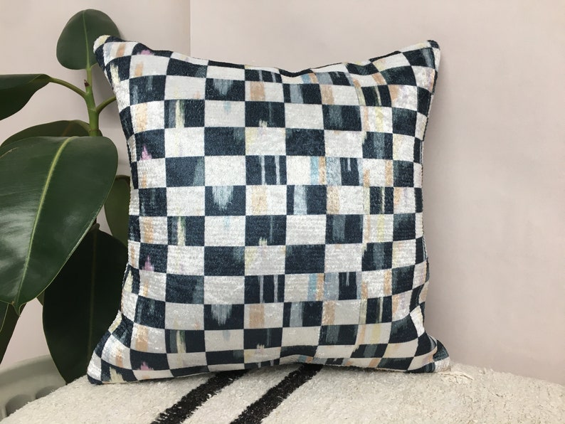 Puede incluir: Una almohada de tiro de cuadros negros y blancos con un sutil brillo iridiscente. La almohada tiene un patr&oacute;n geom&eacute;trico con toques de azul, rosa y amarillo.