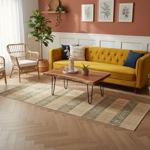 May include: A rectangular area rug featuring a repeating pattern of wide beige stripes alternating with narrower, textured olive green bands with intricate geometric motifs, laid out on a light brown herringbone patterned wooden floor.