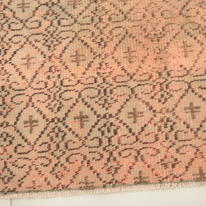 May include: Close-up of a pink and brown patterned rug with a fringe border. The rug has a geometric design with a repeating pattern of diamonds and crosses.