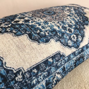 Op de afbeelding: Close-up van een decoratief kussen met een blauw en wit patroon. Het kussen heeft een traditioneel tapijtachtig patroon met ingewikkelde bloemen en geometrische details. Het kleurenpalet omvat tinten blauw, wit en een vleugje bruin.