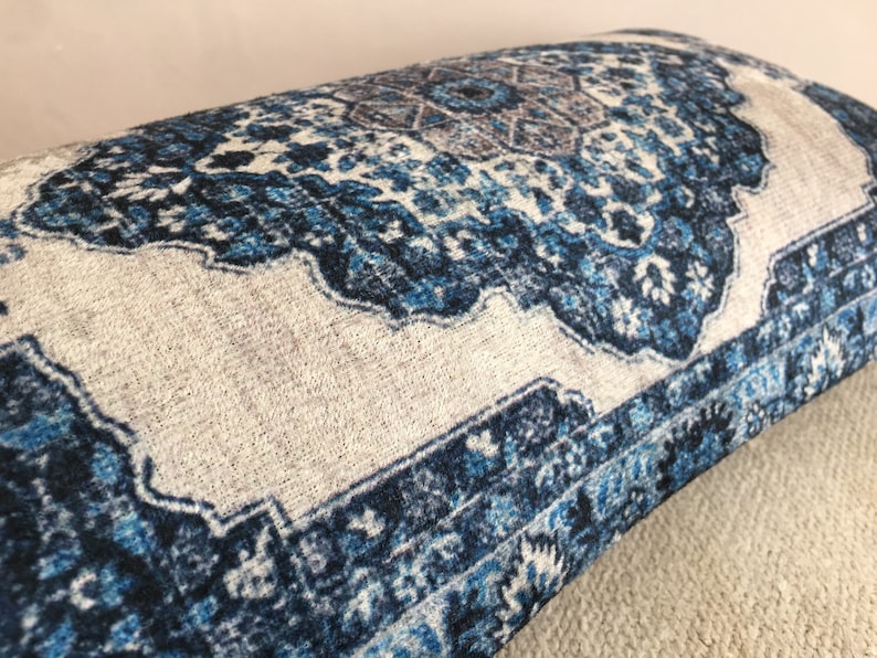 Op de afbeelding: Close-up van een decoratief kussen met een blauw en wit patroon. Het kussen heeft een traditioneel tapijtachtig patroon met ingewikkelde bloemen en geometrische details. Het kleurenpalet omvat tinten blauw, wit en een vleugje bruin.