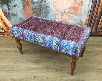 May include: A rectangular upholstered bench featuring a central panel of textured dark maroon fabric surrounded by a border of blue fabric with intricate white and gold geometric patterns, supported by four turned wooden legs in a medium brown finish.