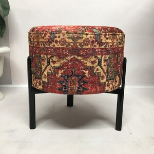 May include: A round ottoman with a red, yellow and blue patterned fabric cover and black wooden legs.