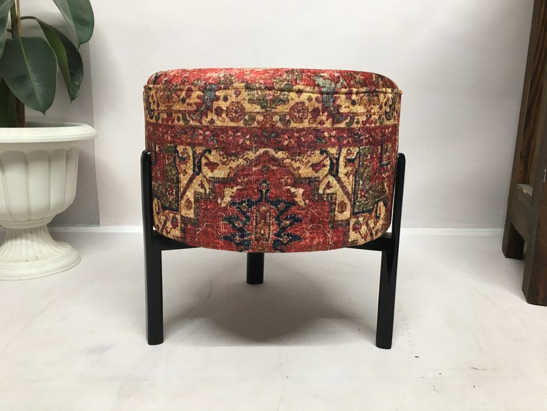 May include: A round ottoman with a red, yellow and blue patterned fabric cover and black wooden legs.