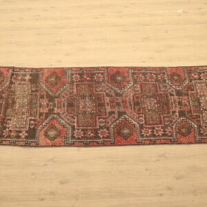 a large, intricately patterned rug with a geometric design in shades of red, black, and white, laid out on a wooden floor.