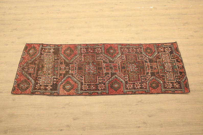 a large, intricately patterned rug with a geometric design in shades of red, black, and white, laid out on a wooden floor.