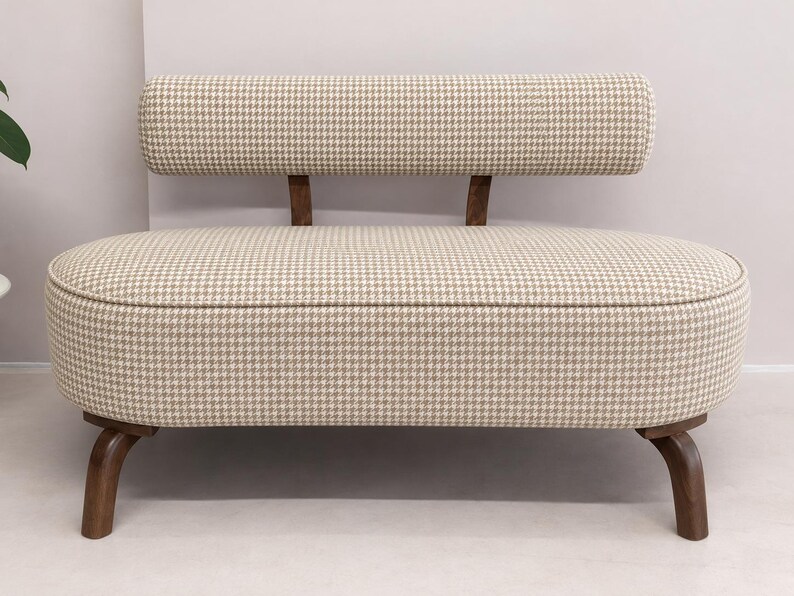 May include: A small loveseat featuring a beige and white houndstooth fabric upholstery. The piece has a rounded, oval-shaped seat and a matching cylindrical backrest supported by two dark brown wooden legs and two wooden back supports.