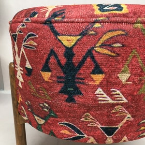 Puede incluir: Un puf redondo rojo con un patr&oacute;n geom&eacute;trico en tonos de amarillo, naranja, verde, azul y negro. El puf est&aacute; tapizado en una tela texturizada y tiene un marco de madera.