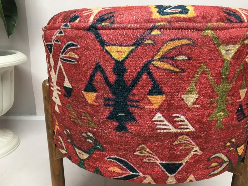 Puede incluir: Un puf redondo rojo con un patr&oacute;n geom&eacute;trico en tonos de amarillo, naranja, verde, azul y negro. El puf est&aacute; tapizado en una tela texturizada y tiene un marco de madera.