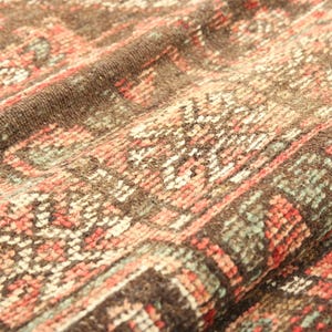 a close-up view of a colorful, intricately patterned fabric, possibly a rug or textile. The fabric has a vibrant mix of red, orange, and green colors, creating a visually striking and detailed design.