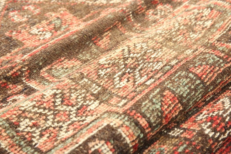 a close-up view of a colorful, intricately patterned fabric, possibly a rug or textile. The fabric has a vibrant mix of red, orange, and green colors, creating a visually striking and detailed design.