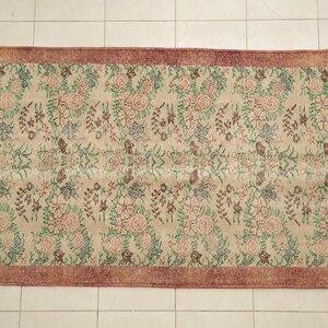 May include: A vintage floral rug with a cream background and a burgundy border. The rug features a repeating pattern of pink, green, and brown flowers.
