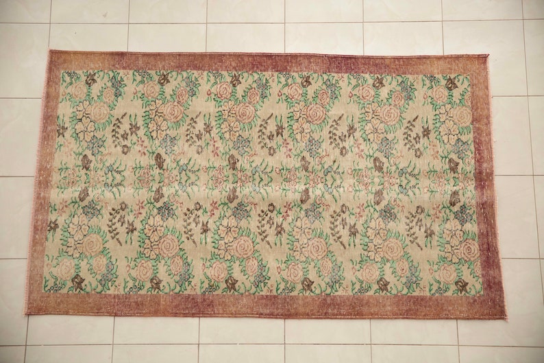 May include: A vintage floral rug with a cream background and a burgundy border. The rug features a repeating pattern of pink, green, and brown flowers.