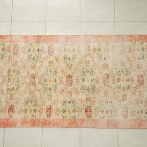 May include: A vintage rug with a floral pattern in shades of pink, green, and yellow. The rug has a faded, distressed look and a peach-colored border.