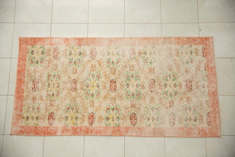 May include: A vintage rug with a floral pattern in shades of pink, green, and yellow. The rug has a faded, distressed look and a peach-colored border.