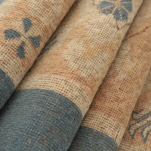 K&ouml;nnte beinhalten: Nahaufnahme eines gewebten Teppichs mit einem beige-blauen Muster. Der Teppich hat eine strukturierte Oberfl&auml;che und ist in mehreren Schichten gefaltet.