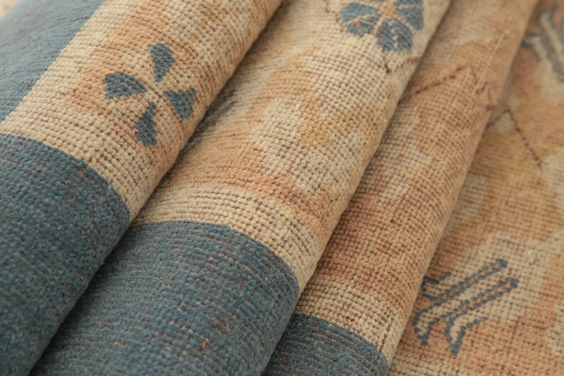 K&ouml;nnte beinhalten: Nahaufnahme eines gewebten Teppichs mit einem beige-blauen Muster. Der Teppich hat eine strukturierte Oberfl&auml;che und ist in mehreren Schichten gefaltet.