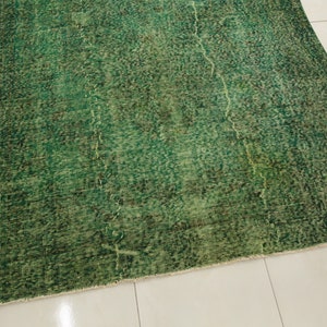 K&ouml;nnte beinhalten: Ein gr&uuml;ner Vintage-Teppich mit einem abgenutzten, verblassten Look. Der Teppich hat ein dezentes Muster und einen Fransenrand.