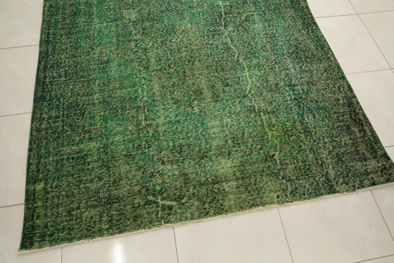 K&ouml;nnte beinhalten: Ein gr&uuml;ner Vintage-Teppich mit einem abgenutzten, verblassten Look. Der Teppich hat ein dezentes Muster und einen Fransenrand.