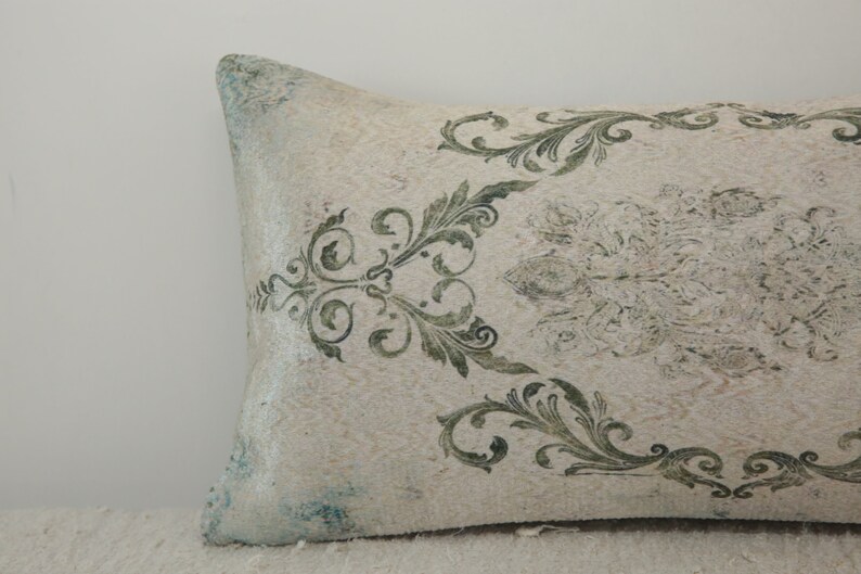 Puede incluir: Una almohada blanca con un patr&oacute;n floral verde y blanco. La almohada est&aacute; hecha de una tela suave y texturizada.