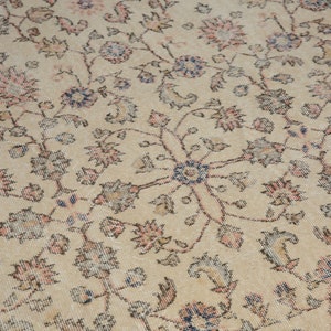 May include: A beige rug with a floral pattern in shades of pink, blue, and brown. The rug has a distressed look, with some of the colors faded.