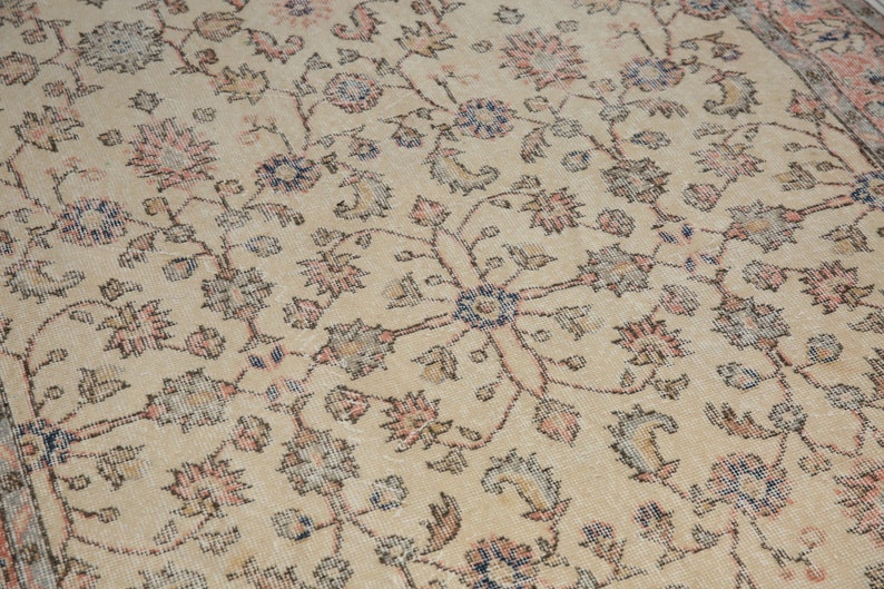 May include: A beige rug with a floral pattern in shades of pink, blue, and brown. The rug has a distressed look, with some of the colors faded.