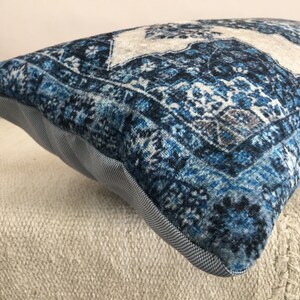 Op de afbeelding: Een rechthoekig decoratief kussen met een blauw en wit patroon. Het kussen heeft een textuur, vintage-stijl patroon met een lichtgrijze rand en een lichtgrijze en witte stof aan de zijkanten.
