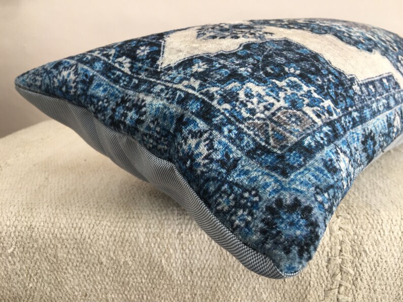 Op de afbeelding: Een rechthoekig decoratief kussen met een blauw en wit patroon. Het kussen heeft een textuur, vintage-stijl patroon met een lichtgrijze rand en een lichtgrijze en witte stof aan de zijkanten.