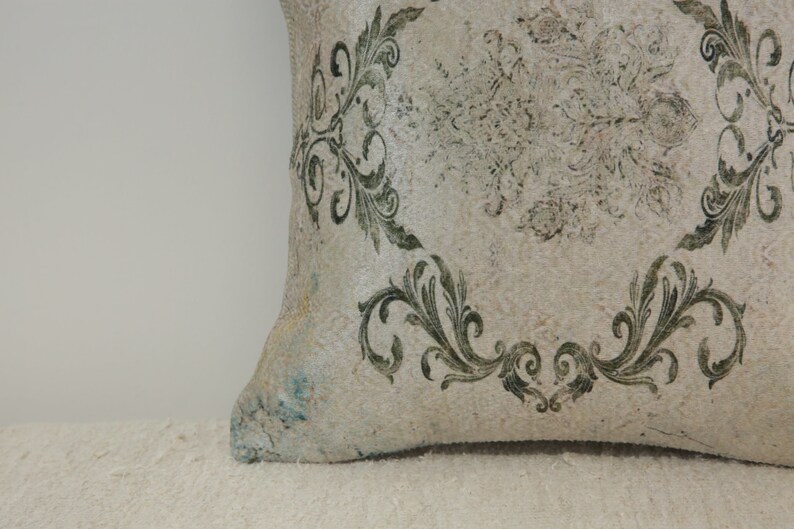 Puede incluir: Una almohada blanca con un patr&oacute;n floral verde. La almohada est&aacute; hecha de una tela texturizada y tiene un aspecto desgastado.