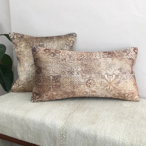 以下が含まれることがあります： 茶色とクリーム色の模様が施された装飾的なクッションが2つ。クッションは薄いベージュ色のソファの上に置かれています。