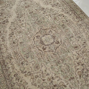 K&ouml;nnte beinhalten: Ein Vintage-Teppich mit beigefarbenem Hintergrund und einem braunen und gr&uuml;nen floralen Muster. Der Teppich hat ein zentrales Medaillon mit einem Sternmuster.