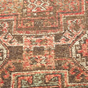 a close-up view of a colorful, intricately patterned rug or carpet with a variety of geometric shapes and designs in shades of red, orange, and green.
