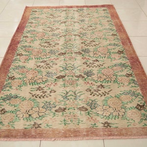 May include: A vintage floral rug with a cream background and a pink border. The rug features a repeating pattern of pink, green, and brown flowers.