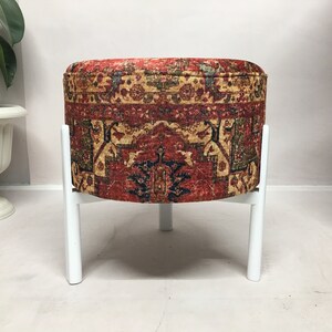 May include: A round, red, white and blue patterned ottoman with a white metal frame. The ottoman is sitting on a white floor.