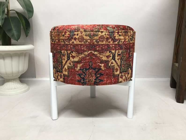May include: A round, red, white and blue patterned ottoman with a white metal frame. The ottoman is sitting on a white floor.
