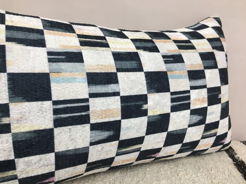Puede incluir: Una almohada de tiro a cuadros en blanco y negro con un sutil brillo iridiscente. La almohada tiene un patr&oacute;n geom&eacute;trico con una ligera variaci&oacute;n en el ancho de las rayas.
