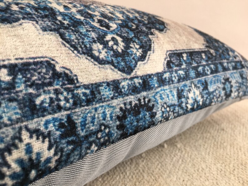 Op de afbeelding: Decoratief kussen met een blauw en wit patroon. Het kussen heeft een gedetailleerd, sierlijk patroon met tinten blauw en wit. Het kussen heeft een grijze stoffen rand.