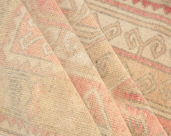 Può includere: Un tappeto tessuto con un motivo geometrico ripetitivo in tonalità tenui di rosa corallo, beige e grigio tenue. Il tessuto presenta una superficie strutturata con bordi lineari intricati e motivi a forma di diamante disposti simmetricamente.