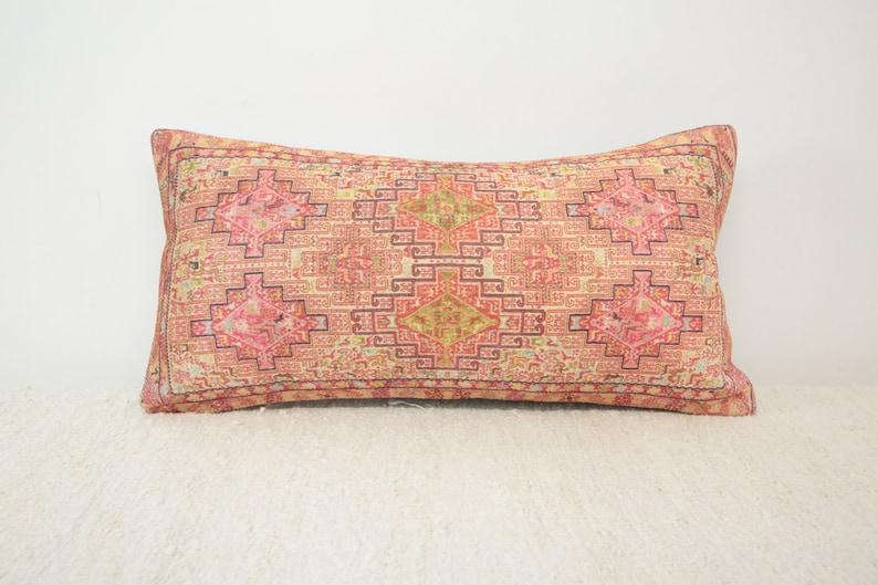 May include: A long rectangular pillow with a pink, red, and yellow geometric pattern. The pillow has a cream-colored background and a dark brown border.