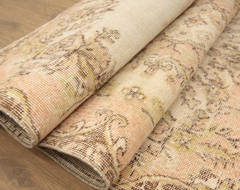 May include: A woven area rug featuring a faded floral pattern in shades of peach, cream, and brown. The rug is partially folded over, revealing the textured weave and the intricate, repeating decorative motifs across its surface.
