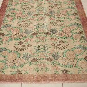 May include: A vintage floral rug with a cream background and a pink border. The rug features a repeating pattern of pink, green, and brown flowers.
