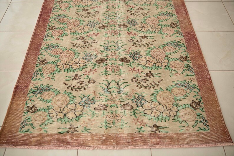 May include: A vintage floral rug with a cream background and a pink border. The rug features a repeating pattern of pink, green, and brown flowers.