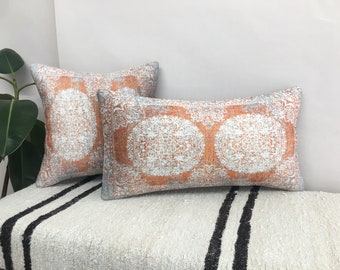 Könnte beinhalten: Zwei dekorative Kissen mit einem weißen und orangefarbenen Muster. Die Kissen liegen auf einer weißen und schwarzen gestreiften Oberfläche.