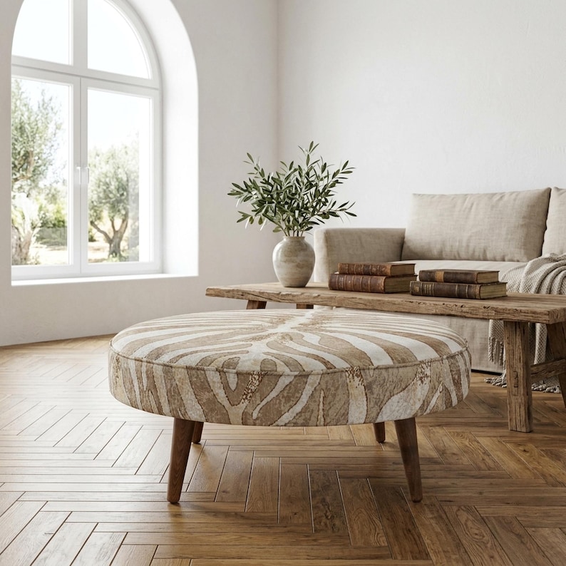 a cozy living room with a large arched window, a wooden coffee table with a zebra print ottoman, a beige sofa, and a vase of greenery.