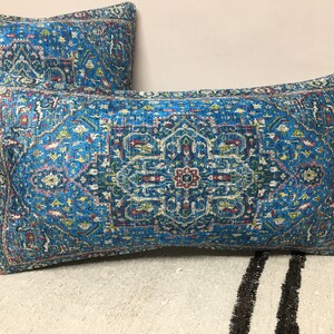 May include: Two blue throw pillows with a colorful geometric pattern. The pillows are on a white and black striped surface.