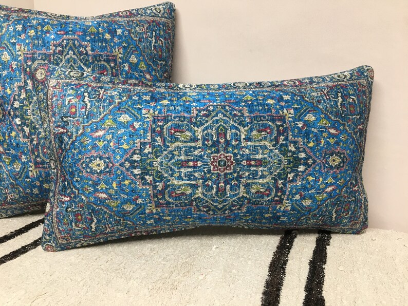 May include: Two blue throw pillows with a colorful geometric pattern. The pillows are on a white and black striped surface.