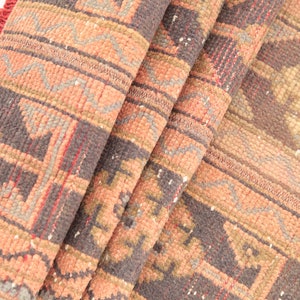 May include: A folded rug with a geometric pattern in shades of pink, brown, and gray. The rug has a fringe border.