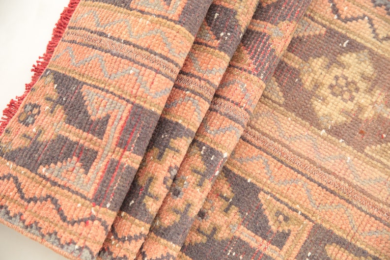 May include: A folded rug with a geometric pattern in shades of pink, brown, and gray. The rug has a fringe border.