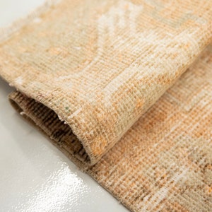 May include: A close-up of a beige and cream woven rug with a subtle pattern. The rug is folded in half, showing the texture of the fabric.